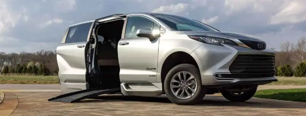 Image of a silver BraunAbility Toyota Sienna hybrid wheelchair van in the driveway of someone's home with its ramp extended and side door open
