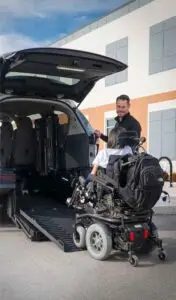 Image of a man talking to a woman in a power wheelchair entering a silver wheelchair van from the rear