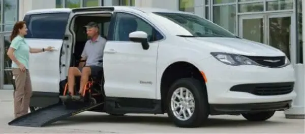 Image of a man coming out of a white chrysler voyager wheelchair van in his manual wheelchair with a lady standing outside