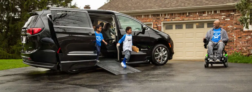 Man in wheelchair in his driveway while his grandkids exit his wheelchair van