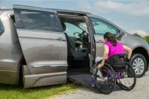 Image of a lady in a manual wheelchair going up the ramp of a silver wheelchair van from BraunAbility in her driveway