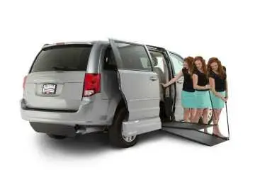 Progressive movement Image of a lady standing outside a silver Dodge Caravan wheelchair van pulling the wheelchair ramp from the vehicle