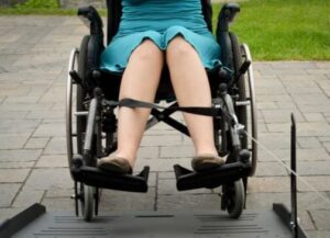 Closeup image of a lady in a blue dress in a wheelchair with a cable from a power pull wheelchair assist helping to pull her up her wheelchair ramp in her vehicle