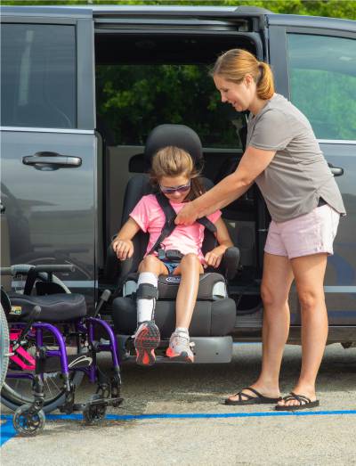 Image of a mom and her daughter exiting their minivan. The mom is standing and the daughter is sitting on her Turny EVO swivel seat about to exit and transfer into her wheelchair