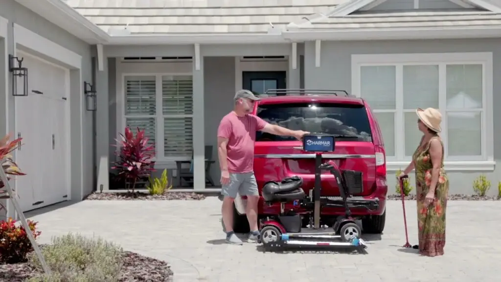 Man and lady standing behind their red minivan in their driveway operating their harmar AL300 scooter lift