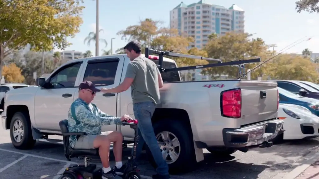 Man on mobility scooter next to a silver pickup truck with a harmar hoist truck lift