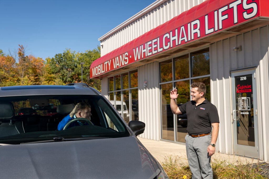 man waving at driver of mobility vehicle outside superior storefront